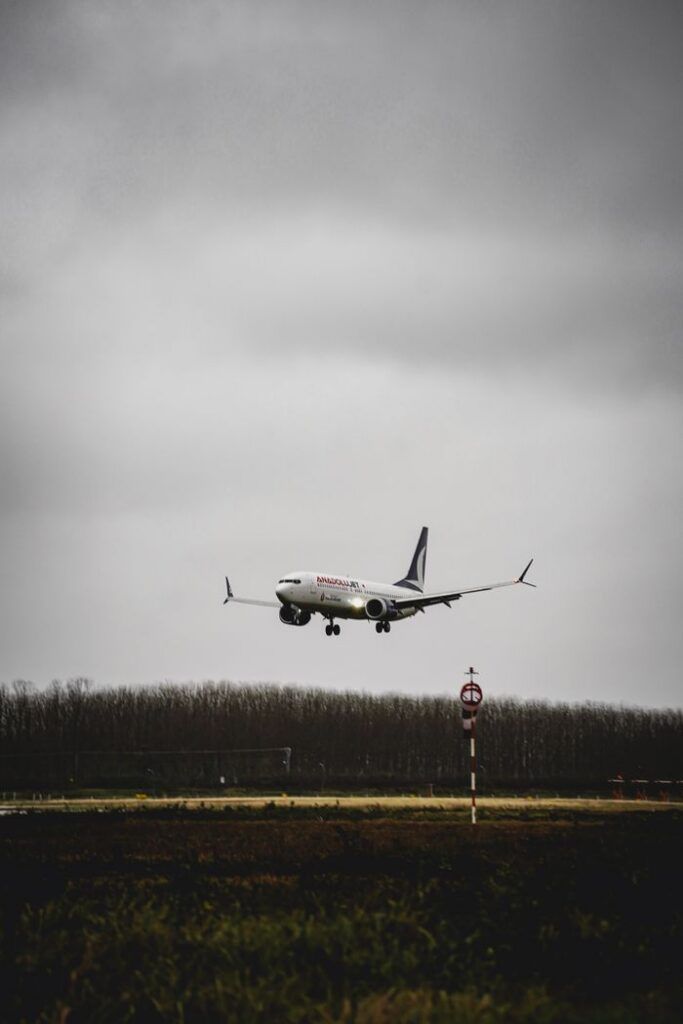 A commercial airplane descends onto a runway against a backdrop of cloudy, overcast skies and distant tree line.